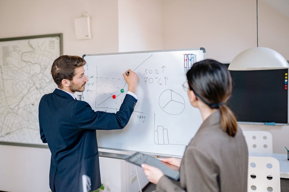 Two business professionals planning and discussing strategy at a whiteboard in a modern office setting.